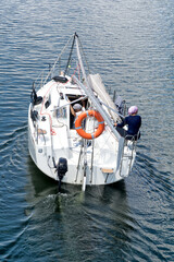 A sailboat maneuvers powered by the engine without sails, with the mast lowered, rear view. Two sailors on board. Leasure, travelling, vacations.