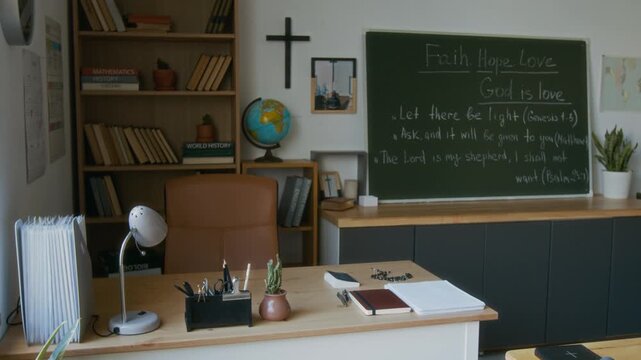 No people shot of classroom interior in modern Christian school with teachers desk, crucifix on wall and Bible quotes on chalkboard