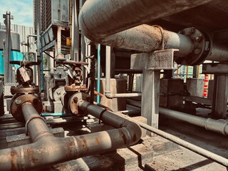 An old industrial piping system with control valves and two heavily rusted exhaust hoods on the...