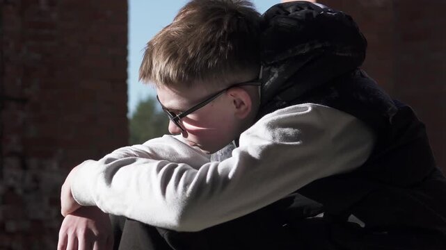 A teenager sits sadly in an abandoned building after being bullied at school. Childhood depression and migraine concept.