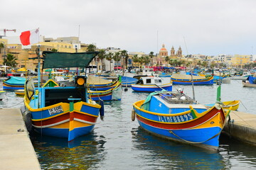 Obraz premium BIRZEBBUGA, MALTA - May 25, 2023: the Colourful small fishing boats moored with buoys in St George's Bay, in Birzebbuga, Malta. This was on a hot sunny day. This is a very traditional town in Malta.