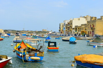 BIRZEBBUGA, MALTA - May 25, 2023: the Colourful small fishing boats moored with buoys in St George's Bay, in Birzebbuga, Malta. This was on a hot sunny day. This is a very traditional town in Malta.