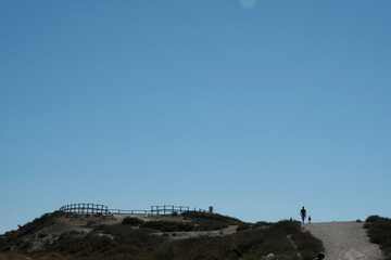 Two hikers walking across an open trail under a vast blue sky. A minimalist scene in the French...