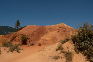Striking red rock formations in the hills of Provence, France, under a clear blue sky. A colorful...