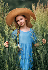 Portrait of a girl kid in a straw hat is standing in in a wheat field in summer.