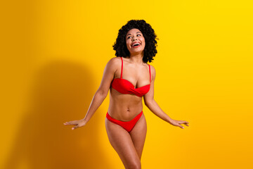 Joyful woman in red bikini radiating happiness against yellow background, embracing summer vibes...