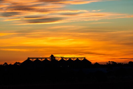 A silhouette of industrial building under the vibrant orange sunset sky with warm hues.