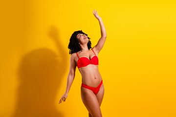 Young woman in vibrant red bikini posing confidently against a bright yellow background showcasing...