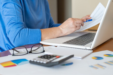 Businesswoman examining financial documents and using a laptop, with charts, calculator, and...