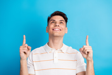 Handsome young man gesturing with index fingers raised against blue background while expressing joy...