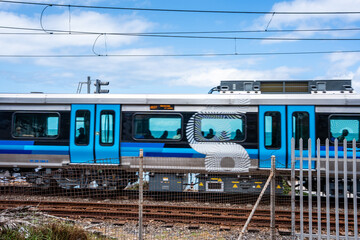 Ein Nahaufnahme eines modernen blauen Zuges, der auf Schienen fährt, mit einem Zaun im Vordergrund...