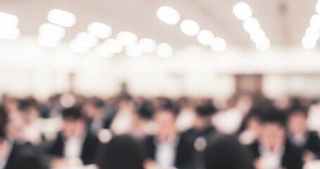 Blurred image shows a crowd of people in a large indoor space.