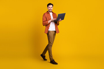 Confident young man with a laptop standing on vibrant yellow background showcasing casual style with trendy fashion