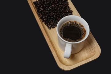 Hot black coffee cup and coffee beans on  wooden tray with black background.