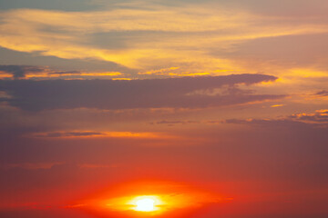 Vibrant dusk with the sun sinking below the horizon. Fiery clouds streak across sky as sun dips below horizon. Layered atmosphere adds depth to the dramatic sunset scene