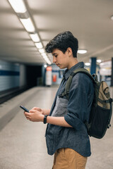 Young student girl using smartphone while waiting for subway train in station