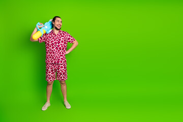 Man wearing pink leopard print outfit holding a water gun, standing on a bright green background...