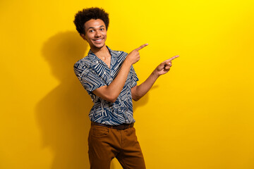 Cheerful young man in casual shirt pointing with his hands on a vibrant yellow background,...