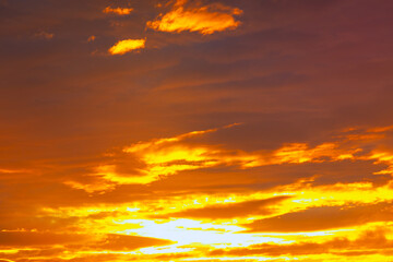 Golden clouds blaze across the twilight sky. Vibrant colors fill the sky as the day transitions to night. Dramatic sunset colors reflected in the clouds