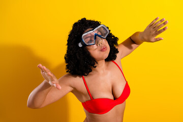 Positive woman in vibrant swimsuit enjoying summer vibes against bright yellow background wearing diving goggles