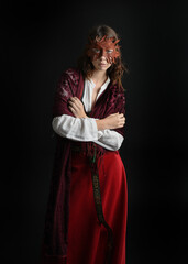 close up portrait of pretty young female brunette  model wearing a fairytale leaf mask and medieval historical gown. Isolated  moody figure on dark studio background.