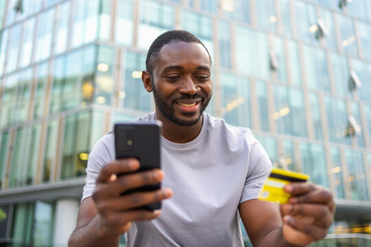 African American man shopping online holding smartphone paying with gold credit card Guy on urban street in city buying on Internet enter credit card details Online shopping ecommerce delivery service
