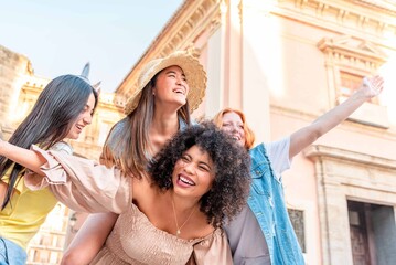 Cheerful multi-ethnic female friends having fun piggybacking in a city, Friendship and youth concept