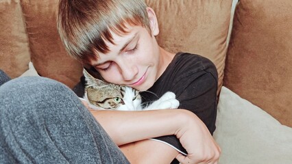 Teenage boy and a cat. Handsome guy hugs his cat while sitting on the couch