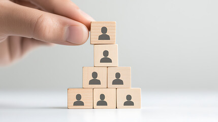 Building a team: Wooden blocks with person icons stacked by a hand representing organizational structure and hierarchy, isolated against a simple background.
