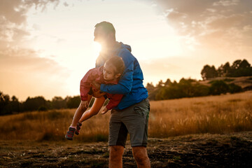 A happy father playing with his daughter, lifting her in the air at sunset. A joyful moment of...
