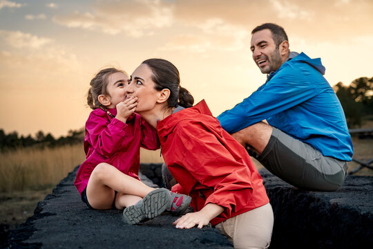 A little girl whispering a secret to her smiling mother in a fun, intimate family moment. A happy family sharing a tender moment of love, trust and complicity outdoors at sunset.