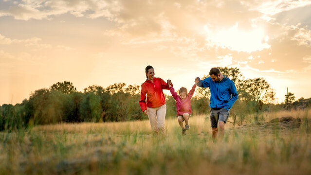 Panoramic web banner of a family playing at sunset, ideal for a website header. Happy parents swinging their daughter in a field, a cinematic image of joy and togetherness.
