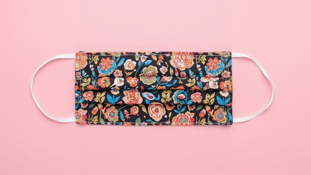 Multicolored homemade cloth face mask displayed on a pink background. Used as a barrier against viruses, pollutants, coughs, and colds.