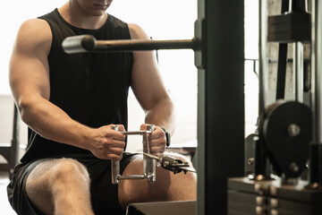 Young caucasian man wearing blank sleeveless tank top exercising on rowing machine at gym. Close up.