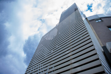 Low-angle view of a contemporary high-rise building with horizontal metal slats and dramatic cloudy...