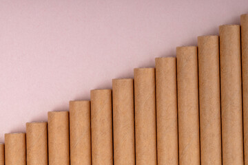 Brown paper straws arranged in a diagonal step pattern on a pastel pink background, symbolizing eco-friendly design and sustainability.
