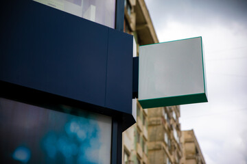 Empty rectangular store sign mounted on modern building with city apartments in background and...