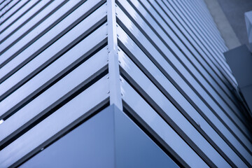 Detailed view of a sharp corner of a building with sleek horizontal metal slats and reflective...