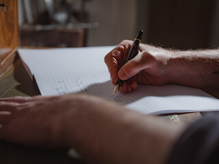 A person's hand holding a pen and writing on a lined notebook