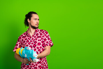Young man in a vibrant pink leopard print shirt holding a water gun and posing confidently against...