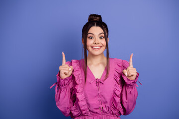 Young woman in a stylish pink ruffled outfit raising fingers with a joyful smile against a vibrant...