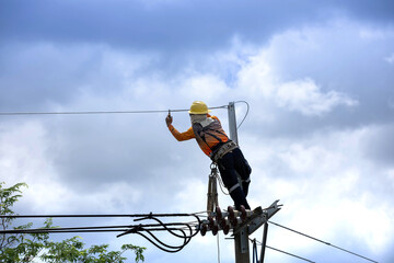 Electric utility technician working on high-voltage power lines atop a utility pole, equipped with...