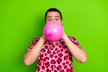 Young man inflating a pink balloon while wearing a stylish leopard print shirt against a bright...