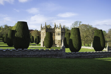 View of a historic Lanhydrock House in the distance, framed by carefully sculpted yew trees and a stone wall under a serene blue sky, Bodmin, England, United Kingdom.