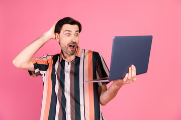 Surprised man in striped shirt holding laptop against pink background showcasing digital excitement...