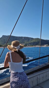 Young woman tourist wearing straw hat, sailing on a boat gazing out the Kiris resort coastline in Turkey. Female enjoying the views as cruising on the deep blue Mediterranean Sea