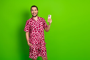 Smiling young man in pink leopard print outfit with phone on vibrant green background showcasing...