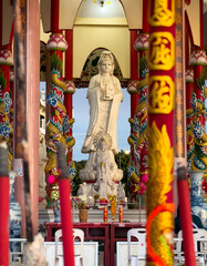 Large statue of Guanyin in colorful temple with dragon columns during sunny afternoon. Sriracha,...