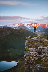 Man traveler hiking solo in Norway standing on cliff edge enjoying sunset mountains and lake view,...