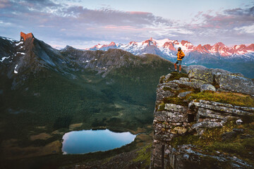 Man traveling in Norway standing on cliff enjoying sunset mountains and lake view traveler hiking...